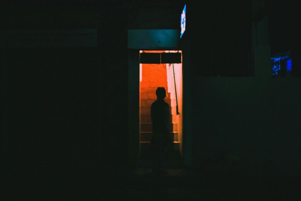 A person stands silhouetted in a red-lit stairway entrance at night.